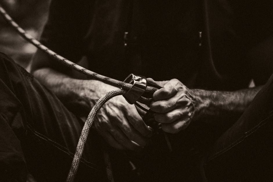 A climber's hands securing a rope with gear, captured in a dramatic sepia tone. Perfect for adventure themes.