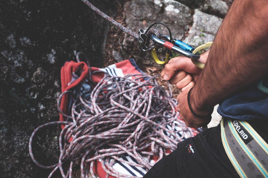 Unrecognizable climber with belay harness with carabines on rope standing near rocky cliff while preparing for mountaineering training in nature